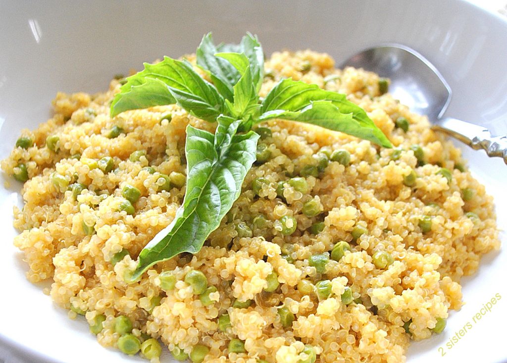 A white bowl filled with cooked quinoa with baby peas and a large fresh basil leaves on top.