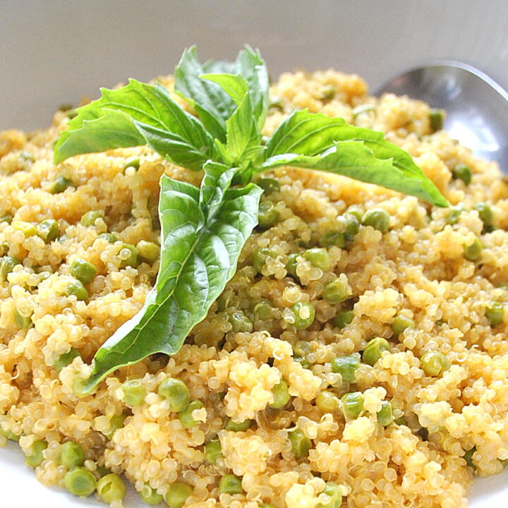 A white bowl filled with cooked quinoa with baby peas and a large fresh basil leaves on top.