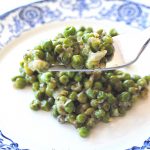 A blue and white plate with a serving of peas and a forkful of baby peas with onions.