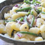 Chunks of boiled potatoes, green beans and sliced red onions, all tossed in a large salad bowl.