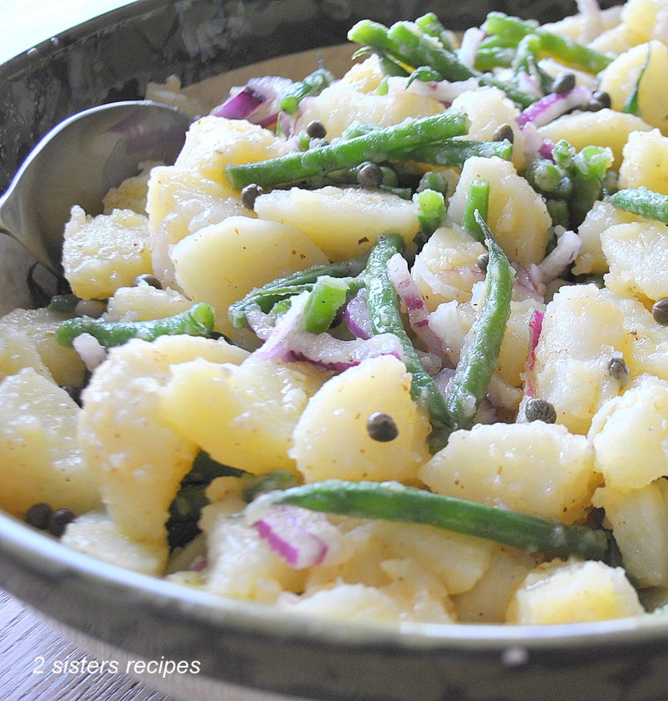 Chunks of boiled potatoes, green beans and sliced red onions, all tossed in a large salad bowl.