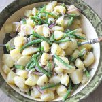 Chunks of boiled potatoes, green beans and sliced red onions, all tossed in a large salad bowl.