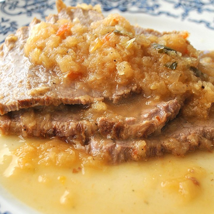 On a white and blue plate is a serving of sliced meat smothered with caramelized onions on top.