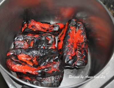 Charred whole red bell peppers resting in a large pot. 