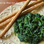Sautéed spinach served on a lovely plate with 3 breadsticks on the side.