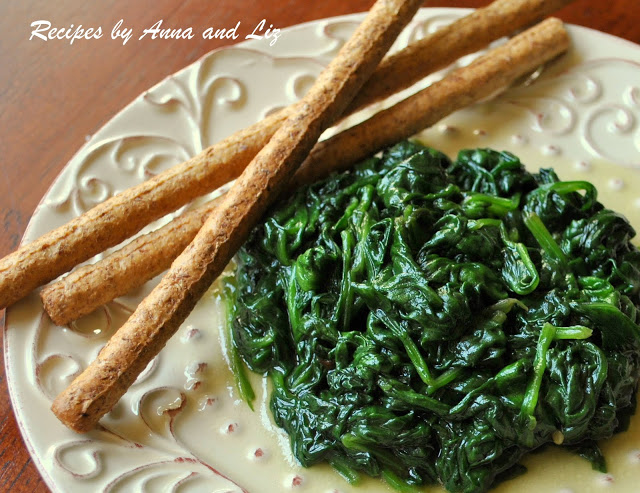 Sautéed spinach served on a lovely plate with 3 breadsticks on the side.