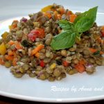 A white plate filled with a lentil salad mixed with chopped colorful peppers and fresh basil leaves on top..
