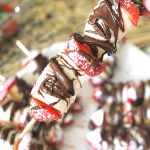 One wood skewer with fresh strawberry and bananas with melted chocolate drizzled on top.
