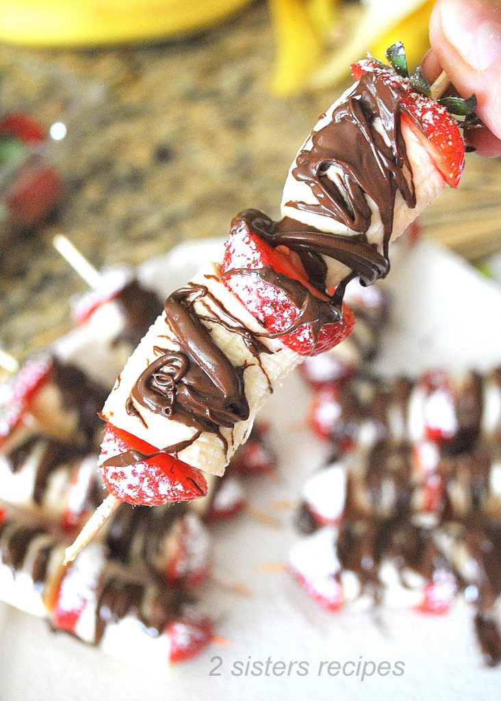 One wood skewer with fresh strawberry and bananas with melted chocolate drizzled on top. 