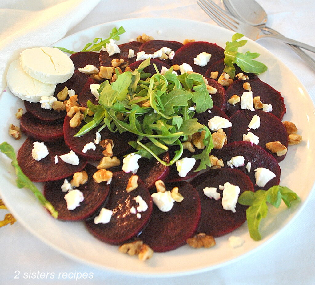 A white plate with a serving of cooked sliced beets, crumbled goat cheese and walnuts on top.