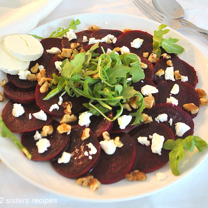 A white plate with a serving of cooked sliced beets, crumbled goat cheese and walnuts on top.