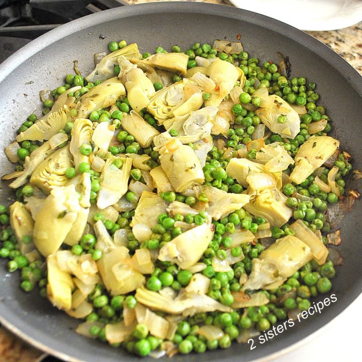 A large skillet sautéing peas and artichoke hearts.