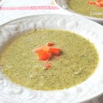 A bowl of creamy broccoli soup with chopped tomatoes on top.