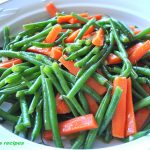 A white serving bowl filled with cooked green beans and carrot sticks.