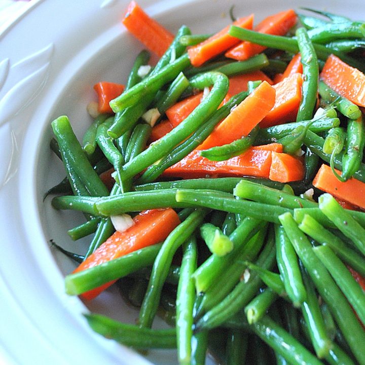 A white ceramic bowl filled with cooked green beans and carrot sticks as a salad.
