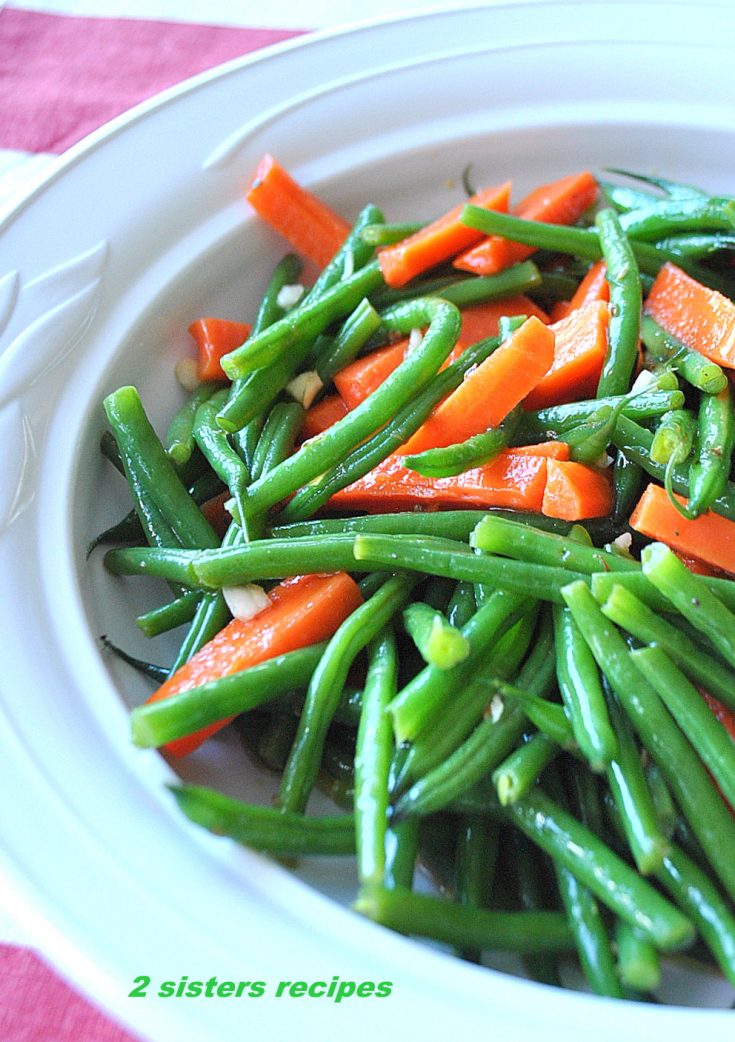 A white ceramic bowl filled with cooked green beans and carrot sticks as a salad.