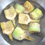 A silver bowl of water filled with already cleaned artichoke hearts.