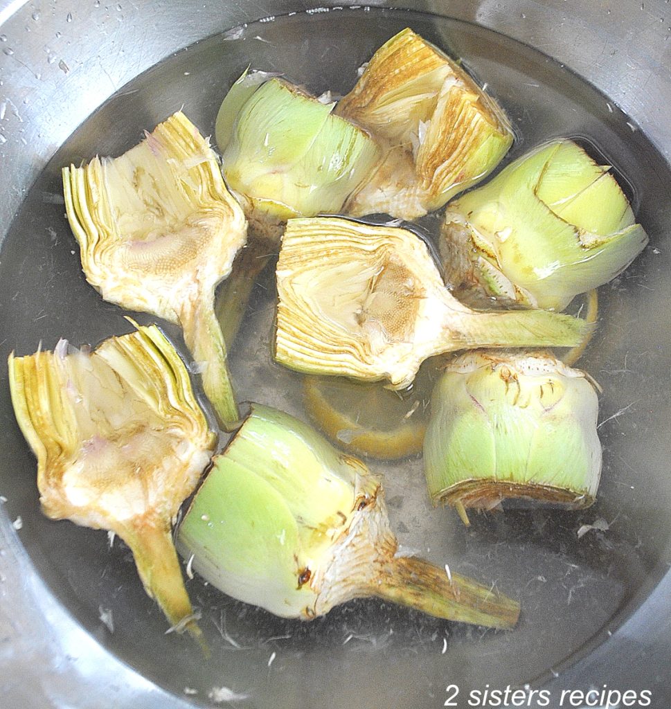 A silver bowl of water filled with already cleaned artichoke hearts.