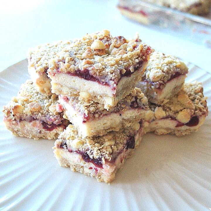 A white cake plate filled with a pile of cranberry cheesecake bars.