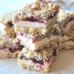 A white cake platter filled with cheesecake and cranberry bars piled on top of one another.