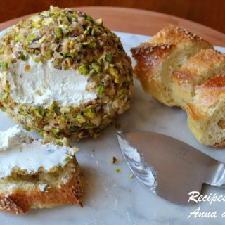 a cheese ball covered in mixed nuts served on a slice of bread,