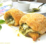 Two baked chicken rolled up and stuffed with pesto and cheese on a white plate.