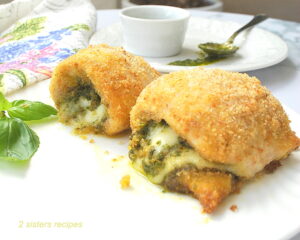 Two baked chicken rolled up and stuffed with pesto and cheese on a white plate.