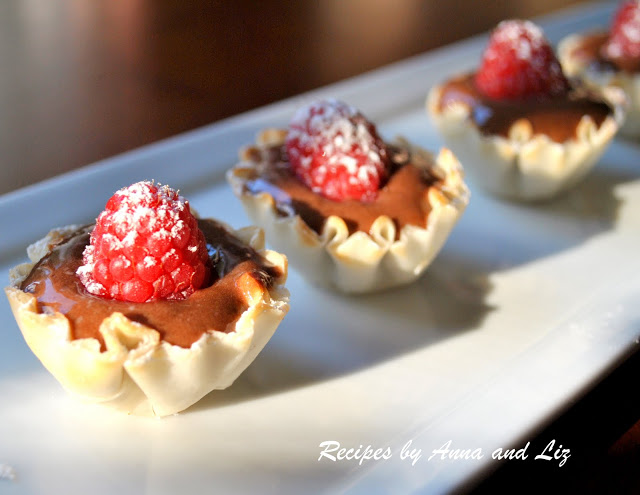 Little fillo pastry cups filled with chocolate pudding and top with raspberry served on a white platter.