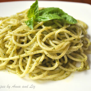 A white plate with a serving of spaghetti tossed with basil pesto sauce.