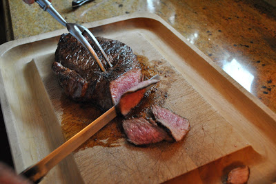 Slicing the grilled London Broil Steak on a wood carving board with a large knife and fork. 