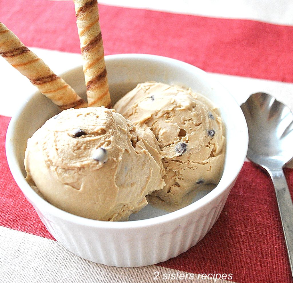  Two scoops of coffee flavored ice cream with two swirls cookies in a small white bowl. 