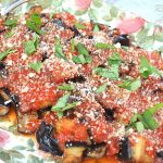 A colorful platter filled with fried eggplant topped with fresh tomato sauce, grated cheese and fresh basil.