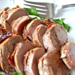 A pork tenderloin sliced and served on a white platter.