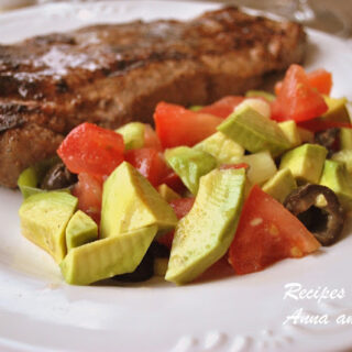 A white dinner plate with a grilled steak and an avocado and tomato salad.