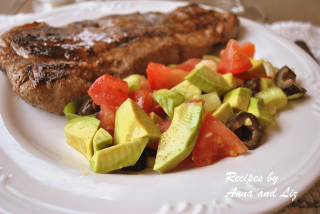 A white dinner plate with a grilled steak and an avocado and tomato salad.