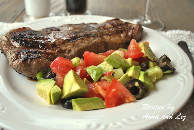 A white dinner plate with a grilled steak and a side of chunky avocado salad.