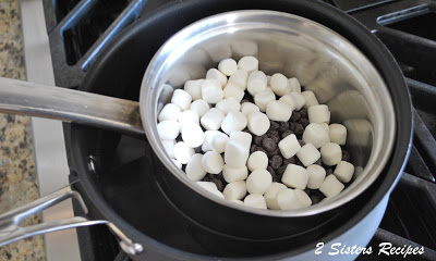 A small pot on stovetop with chocolate chips and small marshmallows