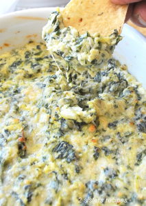 A tortilla chip filled with a spinach and artichoke dip.