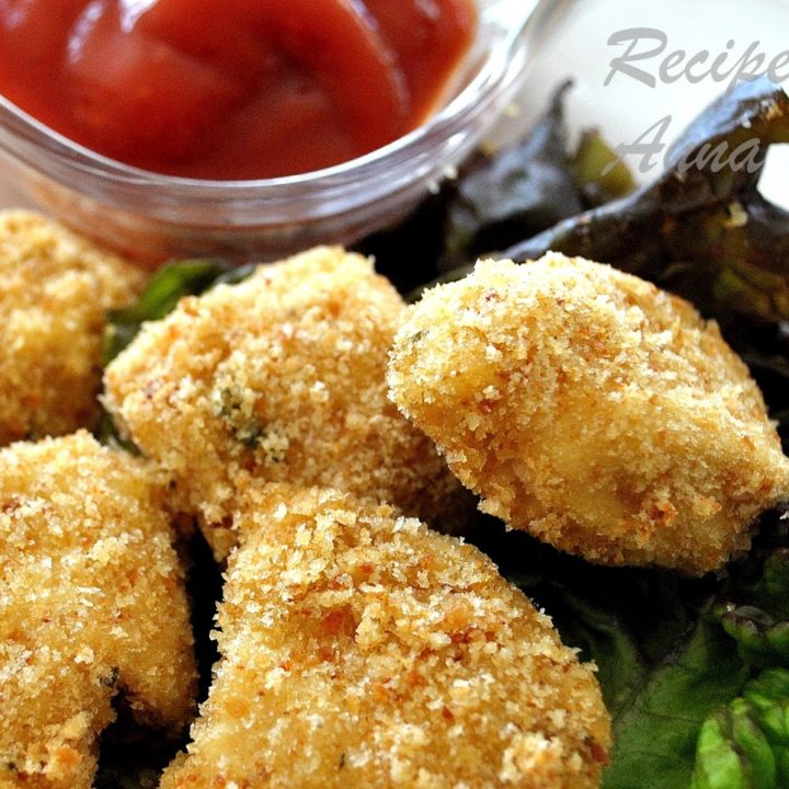 A plate filled with baked chicken nuggets set on a bed of lettuce with bowl of ketchup on the side.