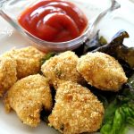 A plate filled with chicken nuggets and a bowl of ketchup on the side.
