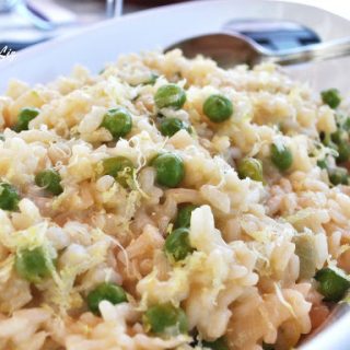 A white oval bowl filled with cooked Italian rice and baby peas.