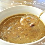 a spoonful of creamy black bean soup served in a white soup bowl.