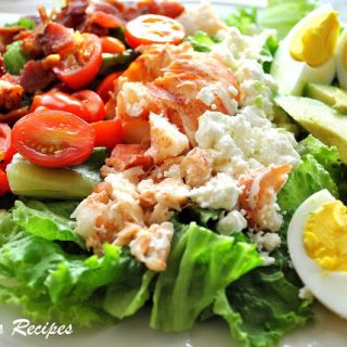a white platter filled with green lettuce, hard boiled eggs, sliced cherry tomatoes and steamed chopped lobster.