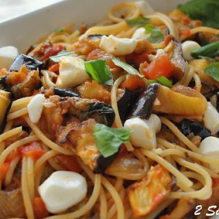 A white oval bowl filled with spaghetti, mini mozzarella balls, chopped eggplant and fresh basil.