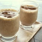 Two small glasses filled with a coffee milkshake topped with some cocoa powder.