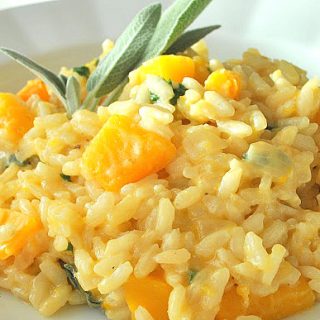 A white bowl filled with cooked Italian rice and chunks of butternut squash and a sage leaf on top.