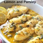 Chicken Tenders Smothered in Lemon and Parsley served in a white oval platter with capers and lemon wedges.