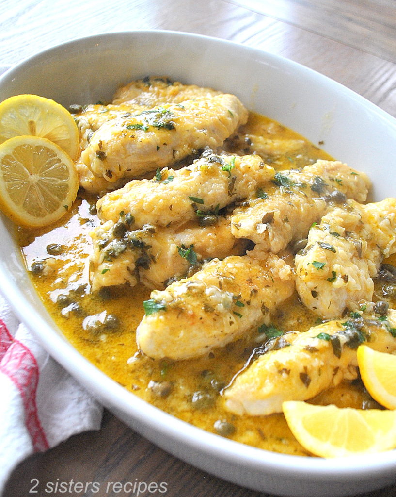 Chicken Tenders Smothered in Lemon and Parsley and served in an oval white dish with lemon slices as garnish. 