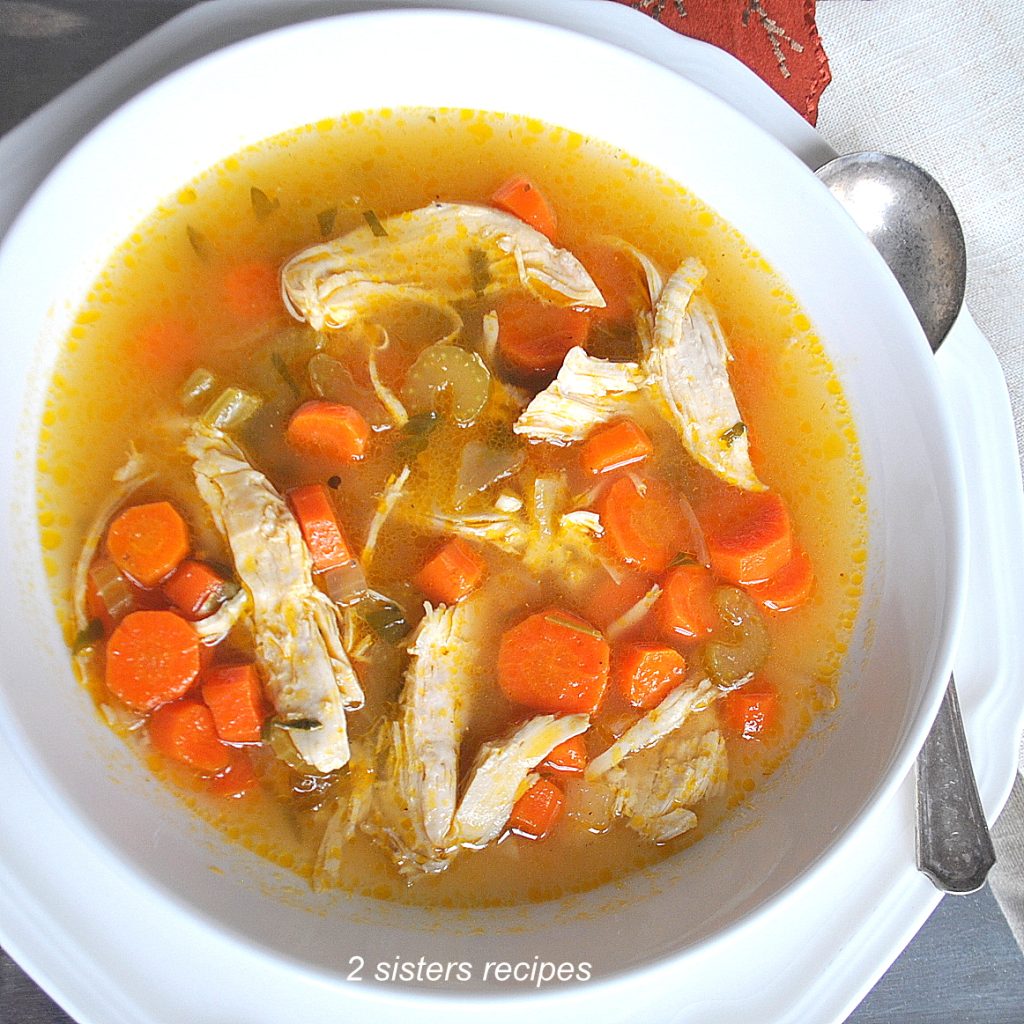A white bowl filled with soup, sliced carrots and leftover turkey meat.
