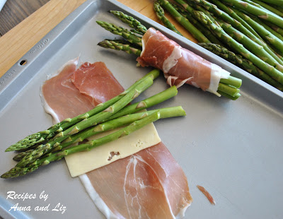  On a baking sheet, a bundle of asparagus being wrapped with cheese and meat. by 2sistersrecipes.com